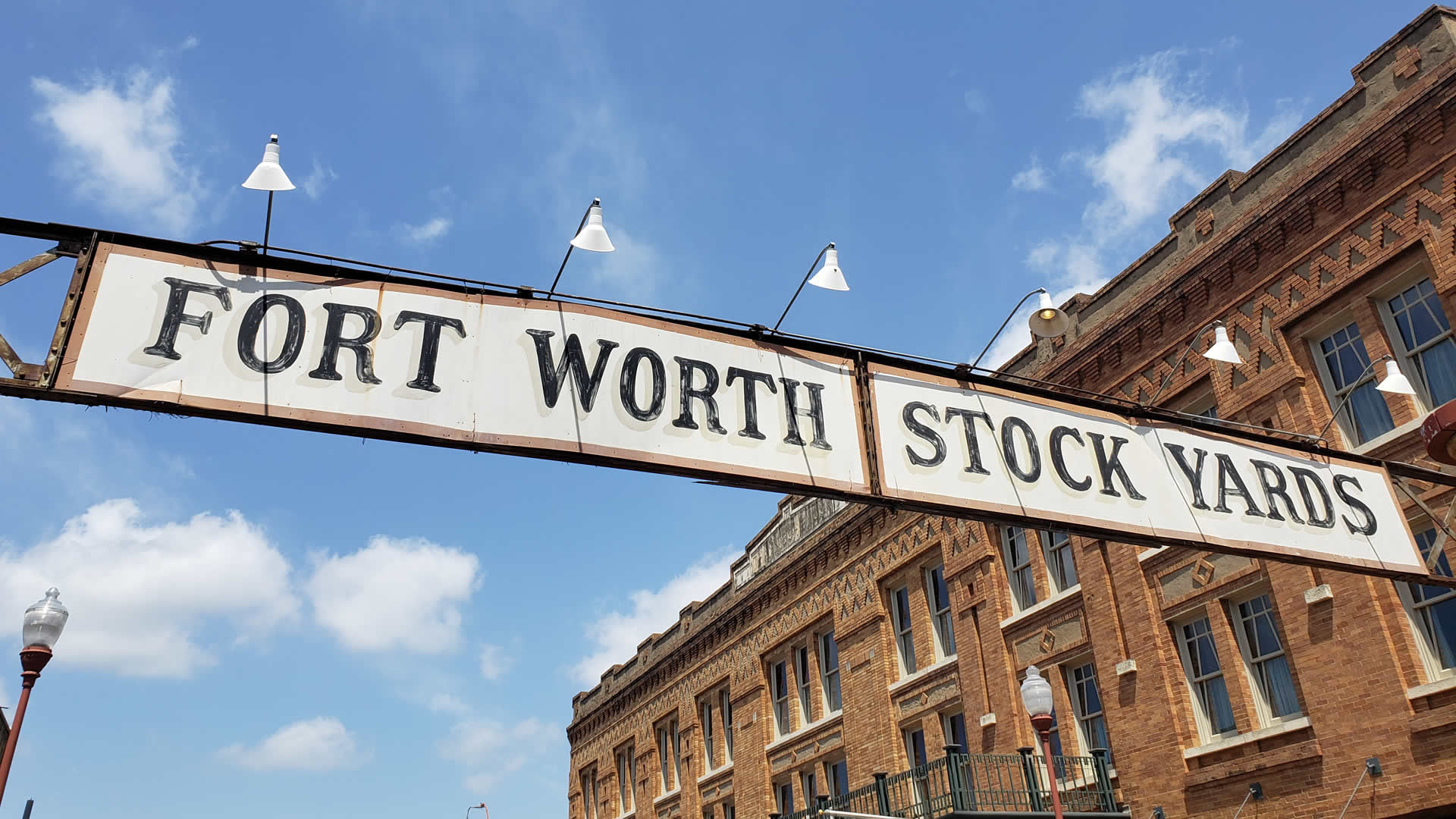 View of Fort Worth Stockyards with historic buildings, cowboy-themed shops, and a Longhorn cattle drive in the heart of the district.